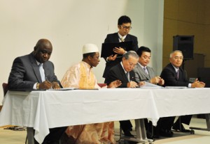 協定書に署名するギニア共和国のセンクン・シラ特命全権大使（左）と徳之島３町長＝19日、伊仙町
