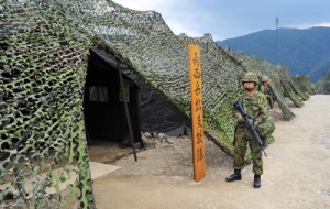 偽装網に覆われた兵站訓練の前進基地（●）と、名瀬港に入港したチャーター船から下船してくる自衛隊車両＝７日、奄美市