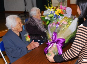 忘年会で花束を受け取る本山イ子さんと松田ミチ子さん（左から）＝３０日、龍郷町秋名