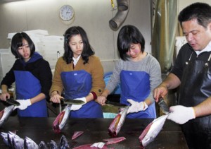 真剣な表情で魚さばき体験に取り組む須磨友が丘高校の生徒ら＝２２日、奄美市名瀬