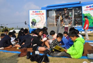 キャラバンカーの周りで思い思いに読書を楽しむ児童ら＝１０日、伊仙町の鹿浦小学校