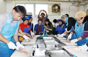 漁師の妻らの手ほどきを受けて魚をさばくツアー参加者＝１４日、奄美市笠利町