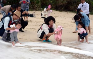 無病息災を祈って海水に子どもの足を浸す母親たち＝２１日、奄美市名瀬の大浜海浜公園