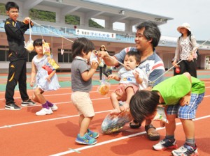 保護者とパン食い競争を楽しむ子どもたち＝２６日、名瀬運動公園陸上競技場