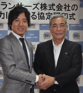 協定調印後に握手を交わす朝山市長（右）と秋好社長＝１日、奄美市役所