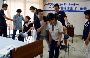 腕を使った起立介助法のこつを教える保田さん（中央）＝２日、奄美市名瀬の生協会館