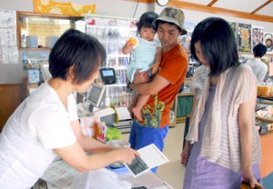 ラリーの説明を受け、チラシにスタンプを押してもらう買い物客（右）＝１８日、奄美市住用町の「サン奄美」