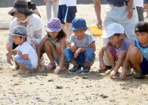 海に向かう子ガメの背中を見守る児童たち＝９日、奄美市笠利町屋仁