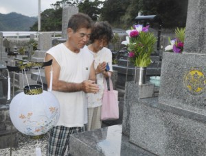 墓前で手を合わせ、先祖の霊を迎える夫婦＝１３日、奄美市名瀬大熊地区の墓地