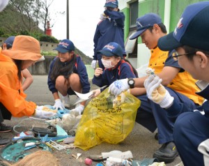  奄美海保の職員と漂着ごみ調査で集めたごみを分類する生徒たち＝２８日、龍郷町の嘉渡海岸