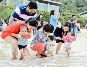 健やかな成長を祈って海水に子どもの足を浸す母親たち＝９日、奄美市名瀬の大浜海浜公園