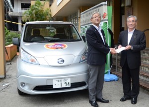 目録を受け取る朝山市長（右）と、貸与された電気自動車＝３０日、奄美市役所