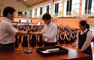 榊署長から指定書を受け取る生徒会の平勝範会長（中央）＝２７日、大島高校体育館