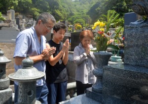 墓前で手を合わせ、先祖らの霊を自宅に伴う家族連れ＝１５日、奄美市名瀬の永田墓地