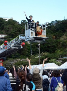 消防はしご車のバスケットに乗って餅をまく朝山市長ら＝８日、伊津部小校庭