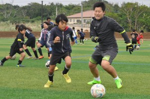 完成した人工芝グラウンドでサッカー元日本代表の海堀さん（右）と競り合う小学生ら＝２５日、与論町　