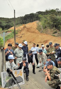 県の担当者から事業の内容について説明を受ける参加者。後方はハード整備が進む現場＝２４日、奄美市名瀬朝日町の浦上川水系総合流域防災事業現場