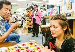 ステージの合間に試食を手伝う澤愛香さん（右）。徳之島の商品をＰＲする高岡町長（中央）＝３日、三越本店