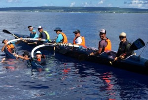 ６人乗りカヌーで奄美大島―喜界島往復横断を達成した参加者。背景は喜界島（提供写真）