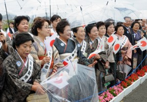 雨の中、紬姿で天皇、皇后両陛下の到着を待つパナウルゆいまぁる会のメンバー＝１７日午前１１時１０分ごろ、与論空港