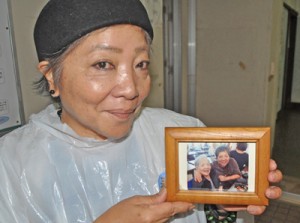 母・山川シズさんとの親子スナップ写真を手に、笑顔を見せる上田さん＝１７日、知名町