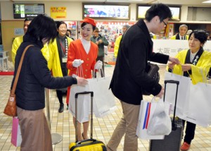 伊丹―奄美大島線の就航４５周年で、開設当時の制服を着て搭乗客に記念品などを配る客室乗務員（中央）ら＝１１日、奄美市笠利町の奄美空港