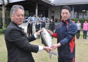 冬季合宿中の実業団チームにカンパチを贈った奄美群島地区漁業士会の田畑会長（左）＝８日、天城町与名間