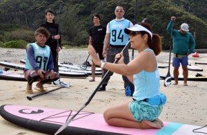 参加者にパドルの持ち方を指導する安さん（右）＝１４日、奄美市名瀬の朝仁海岸