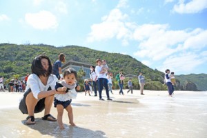 無病息災を祈って海水に子どもの足を浸す家族ら＝１８日、奄美市名瀬の大浜海浜公園