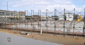 基礎工事が完了し、外部の足場組立て作業などが始まった和泊町の新庁舎建設工事。左の建物が現庁舎＝１１日、同町