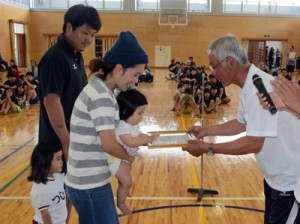 安田区長から賞状と祝い金を受け取る新生児と家族＝５日、宇検村田検中体育館