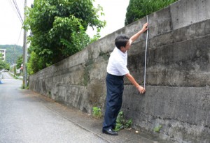 道路に面した学校の塀の高さを測る伊津部小学校の末吉校長＝２１日、奄美市名瀬