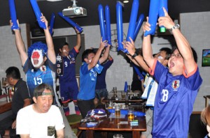 大迫選手のゴールに総立ちで喜ぶ沖永良部サッカー協会の会員ら＝１９日、和泊町