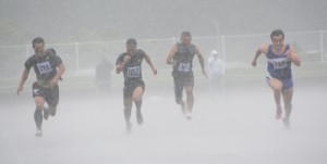 男子４０代１００メートル決勝。激しく降る雨とも戦いながらゴールへ向かう出場選手＝２１日、奄美市の名瀬運動公園陸上競技場