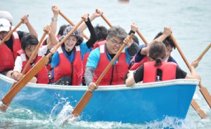 太鼓の音に合わせて懸命にかいをこぐ、くり舟競争の参加者＝２９日、知名町の知名漁港