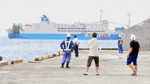  うねりを伴う高波の影響で接岸せずに港を通り過ぎるフェリー。岸壁では待ち受けた港湾関係者らが残念そうに見送った＝２３日、和泊町の伊延港