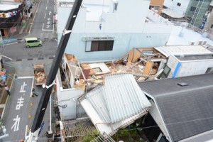 暴風で壊れ、隣接する建物を覆う商業ビルの屋根部分＝２２日午後２時３０分ごろ、奄美市名瀬