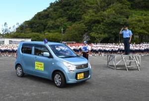 大川署長（右）や児童らに見送られパトロールに向かう青パト車両＝１３日、奄美市名瀬の朝日小学校