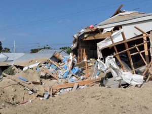 爆風で壊れた倉庫と土砂が吹き飛ばされ穴が開いた現場＝１８日午後２時１５分ごろ、喜界町湾