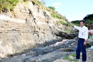 地層がむき出しとなっている「長嶺の島尻層群」を指し示す喜界町企画観光課の富課