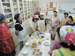 鶏飯の盛り付け方を教える奥田千草さん（左から５人目）、アシスタントの長女千恵さん（同３人目）＝８日、沖縄県那覇市