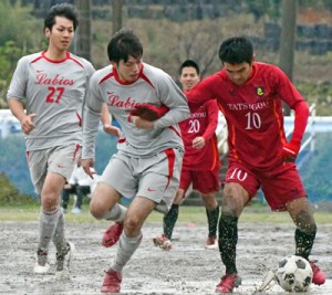 【準々決勝・Ｌａｂｉｏｓ―龍郷クラブ】ぬかるんだグラウンドでボールを競り合う両チームの選手＝９日、龍郷町中央グラウンド