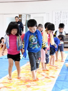 布の上を歩き、足跡をつけてオリジナルアートづくりを体験する園児ら＝１１日、伊仙町犬田布