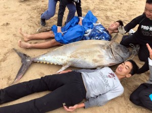 マグロと背比べする２人＝８日、赤木名海岸