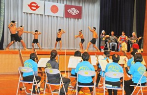 奄美オーケストラの演奏で油井の豊年踊りを踊る児童生徒ら＝１２日、瀬戸内町の油井小中学校体育館