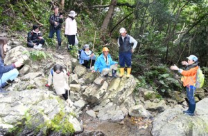  「あい山の滝」について解説する永田さん（右）とプレツアー参加者＝２６日、徳之島町山