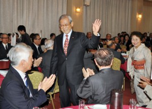 旭日大綬章の受章祝賀会で出席者にあいさつしながら会場入りする保岡元衆院議員（中央）＝１６日、奄美市名瀬