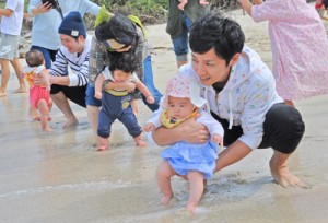 無病息災を祈って子の足を海水に浸す家族ら＝７日、奄美市名瀬の大浜海浜公園