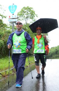 雨の中、奄美大島を元気に歩く（左から）花牟礼さんと塩川さん＝２９日、龍郷町