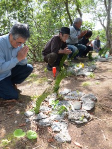 ソテツの葉をささげ、手を合わせる参列者＝１４日、奄美市笠利町